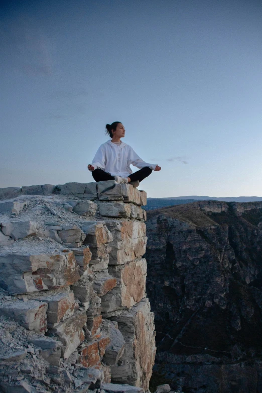 a person with an open jacket on sitting at a rock ledge