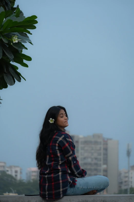 a woman sits on the ledge next to plants and is looking at the sky