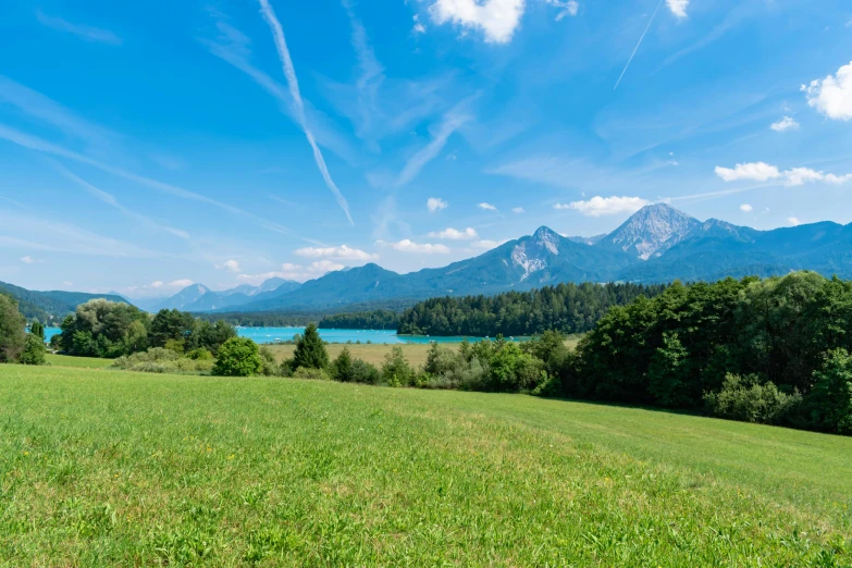 a lush green hillside and green grass area under a cloudy blue sky