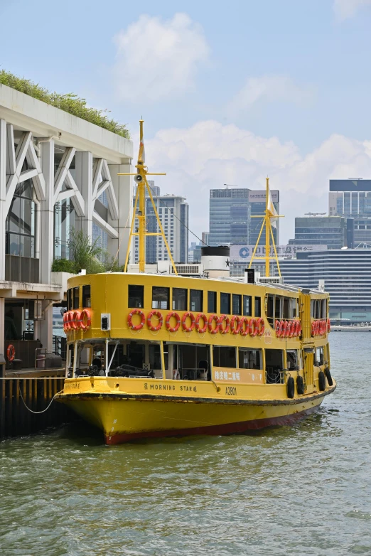 a yellow and red ferry boat with buildings in the background