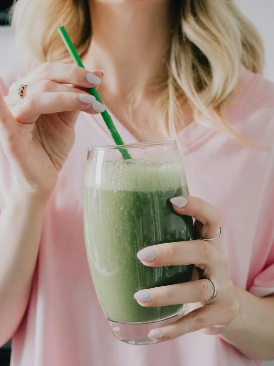 a woman is holding a glass with a green smoothie inside