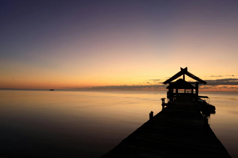 the sun is setting on the lake with a gazebo