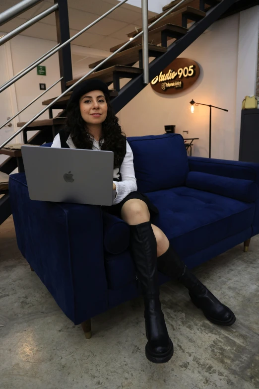 a woman sitting on a blue couch while using a laptop