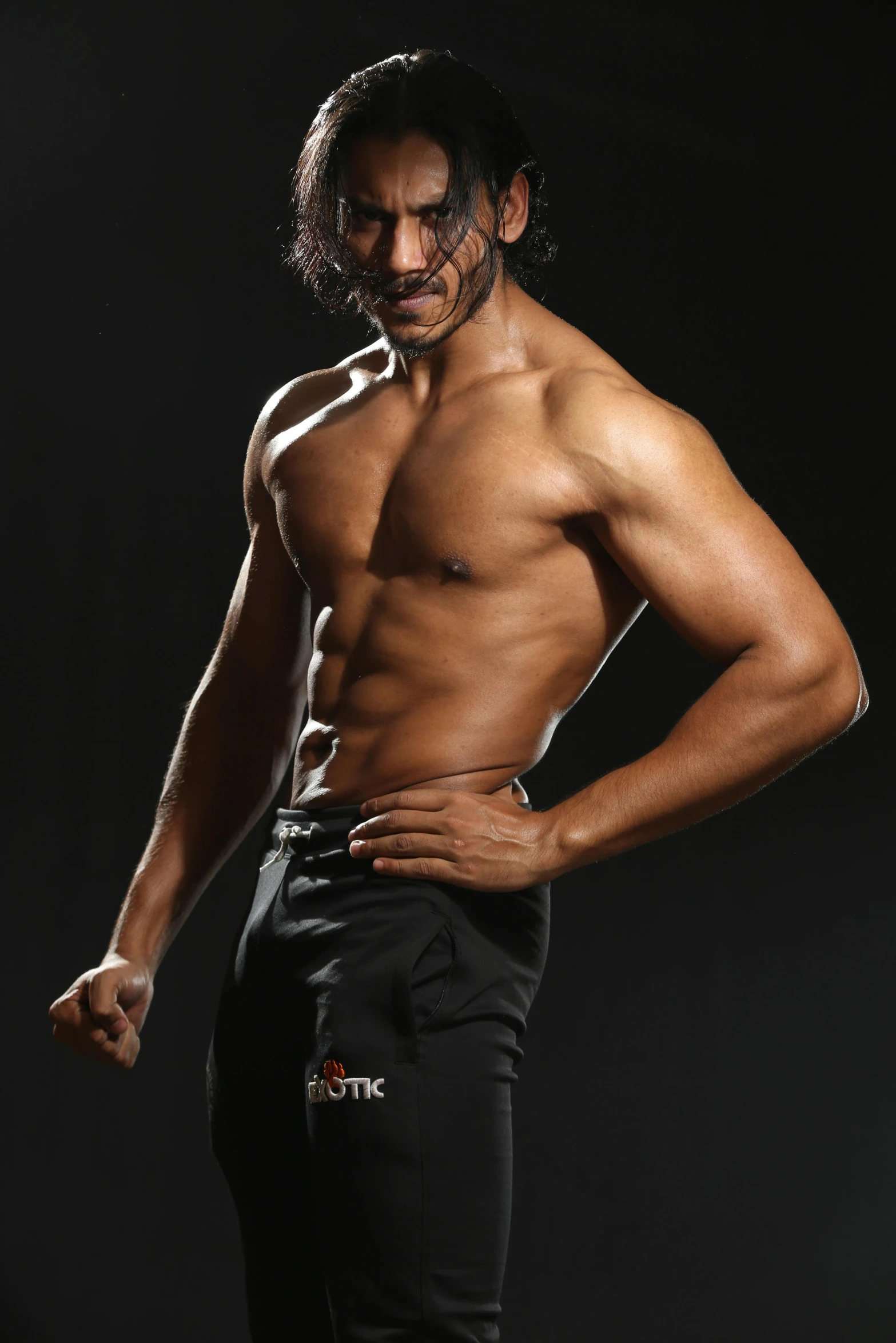 a man is without his shirt standing in front of a black backdrop