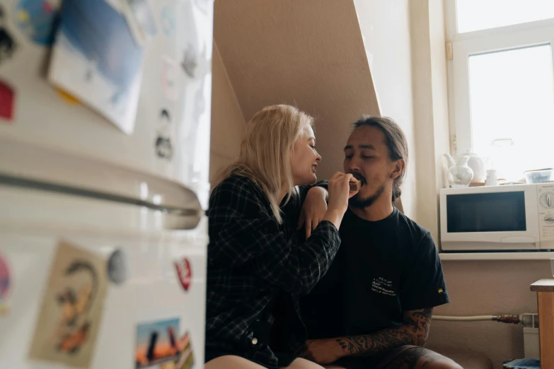 man and woman sitting in a kitchen near a refrigerator