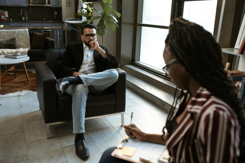 two people sitting in chairs talking while one is holding his hand on his chin