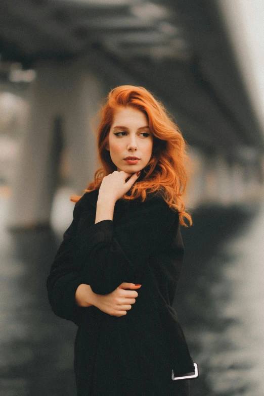 a woman standing on a sidewalk with her hand resting her chin