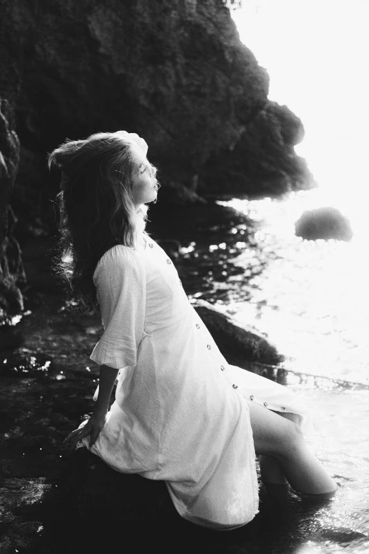a girl in white is sitting on rocks near the ocean