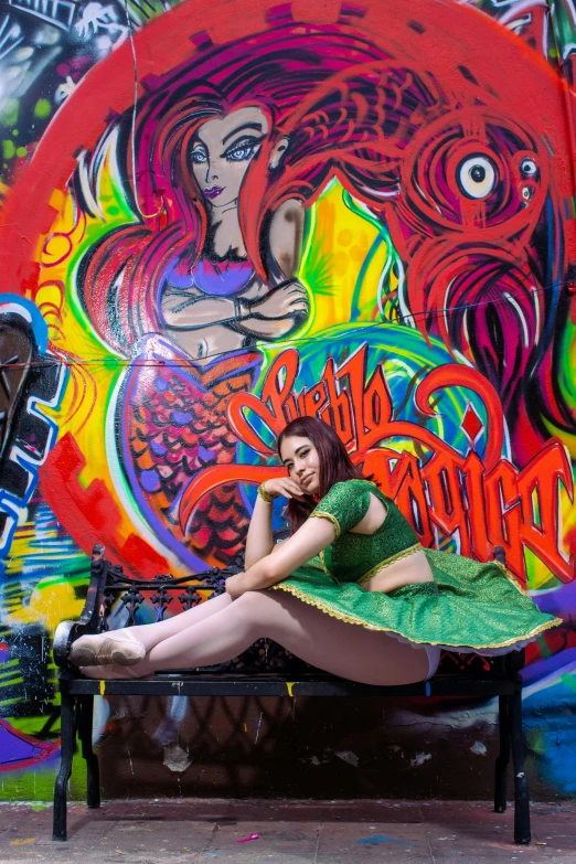 a woman is sitting on a bench under some colorful graffiti