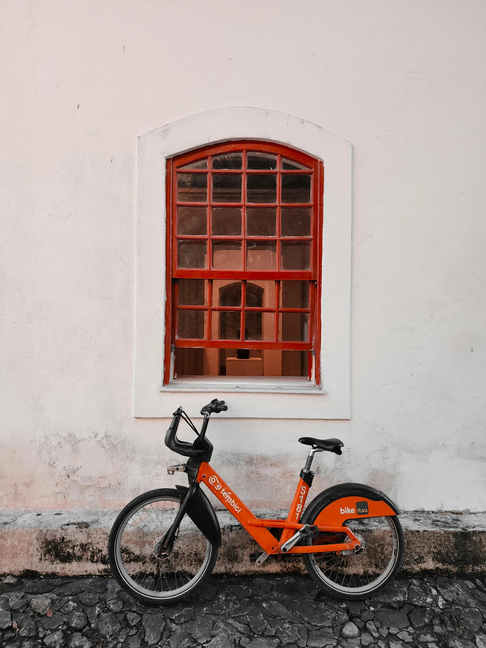 an orange bicycle sits in front of an empty window