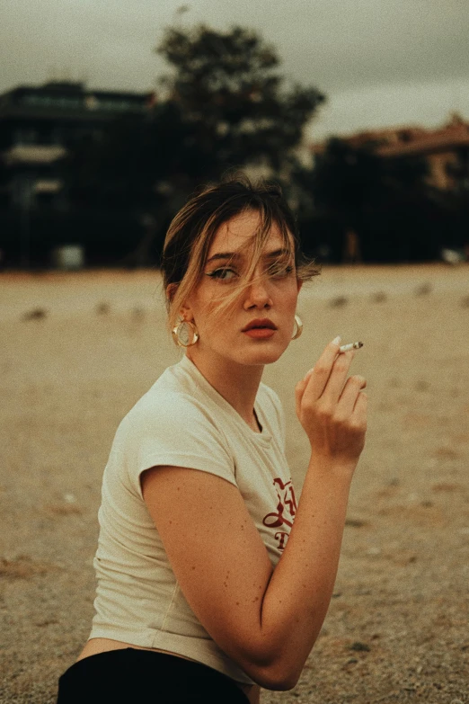 a woman sits in the sand and smokes a cigarette