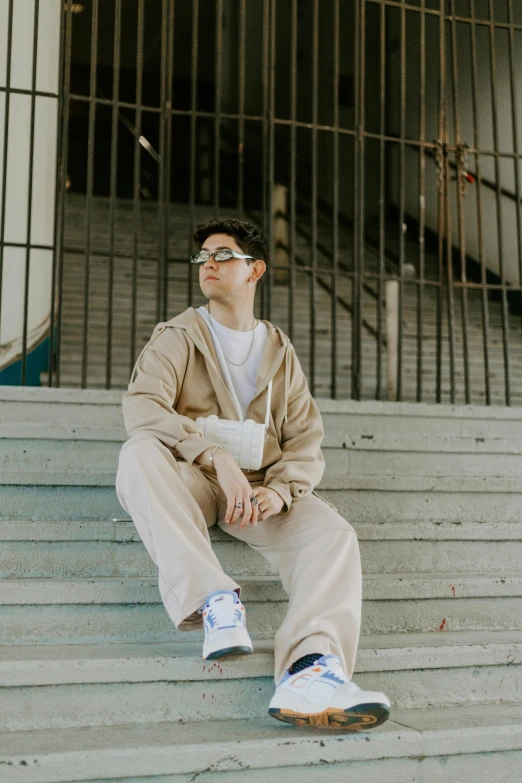 a young man in a tan jacket and sneakers sitting on stairs