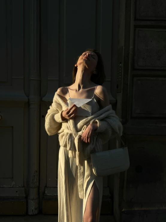 a woman in a long white dress is standing near a wall