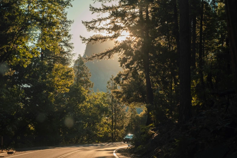a car drives down the road in front of trees and mountains
