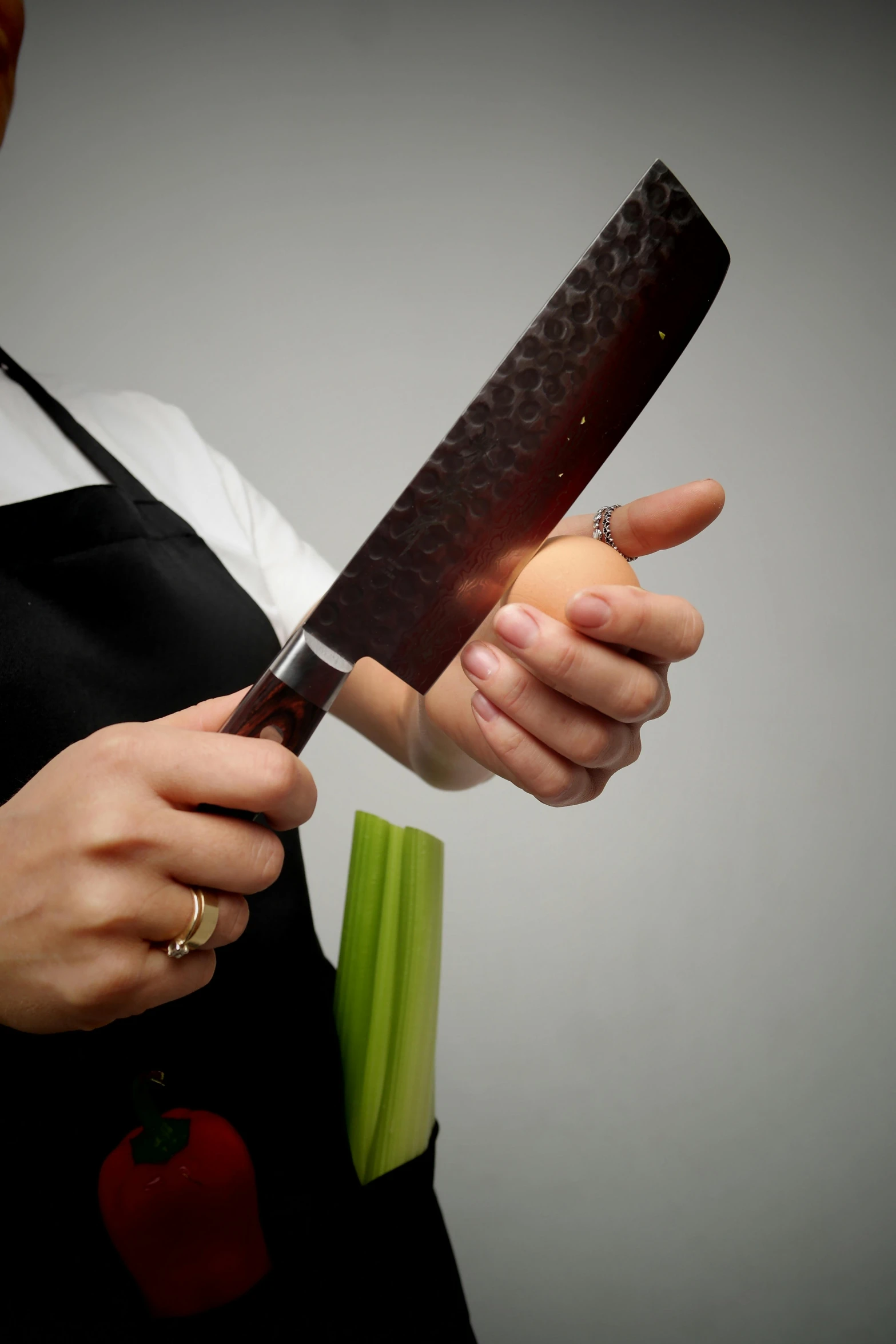 a person with an apron holding a knife near celery