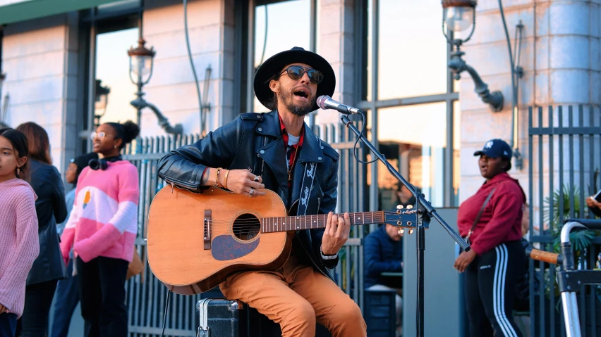 man playing guitar on street in front of a group of people