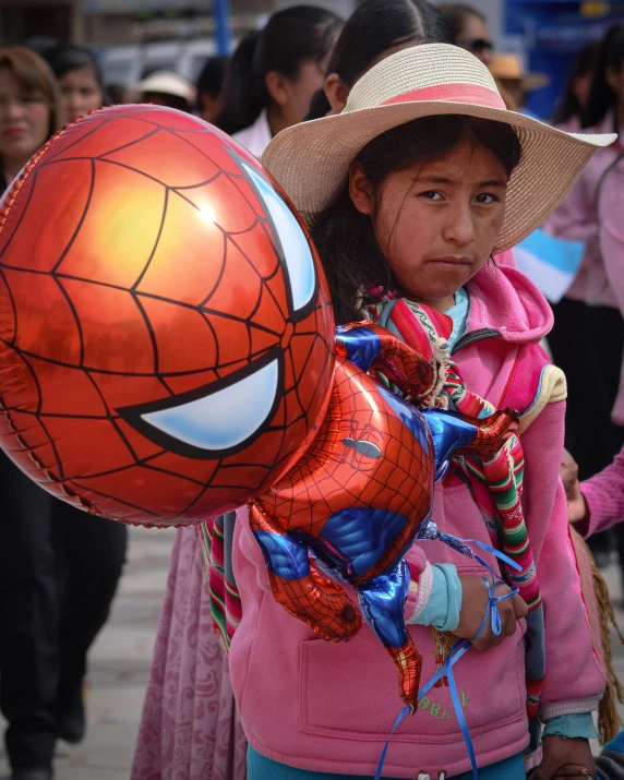 a girl carrying an orange ball and spiderman balloon