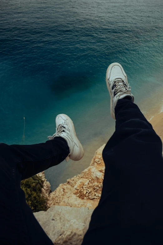 two people in white shoes looking down at the ocean from above