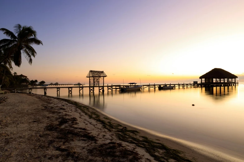 the sun is setting at the pier on a beach