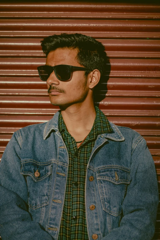 man wearing black sunglasses and a jean jacket looking away from the camera