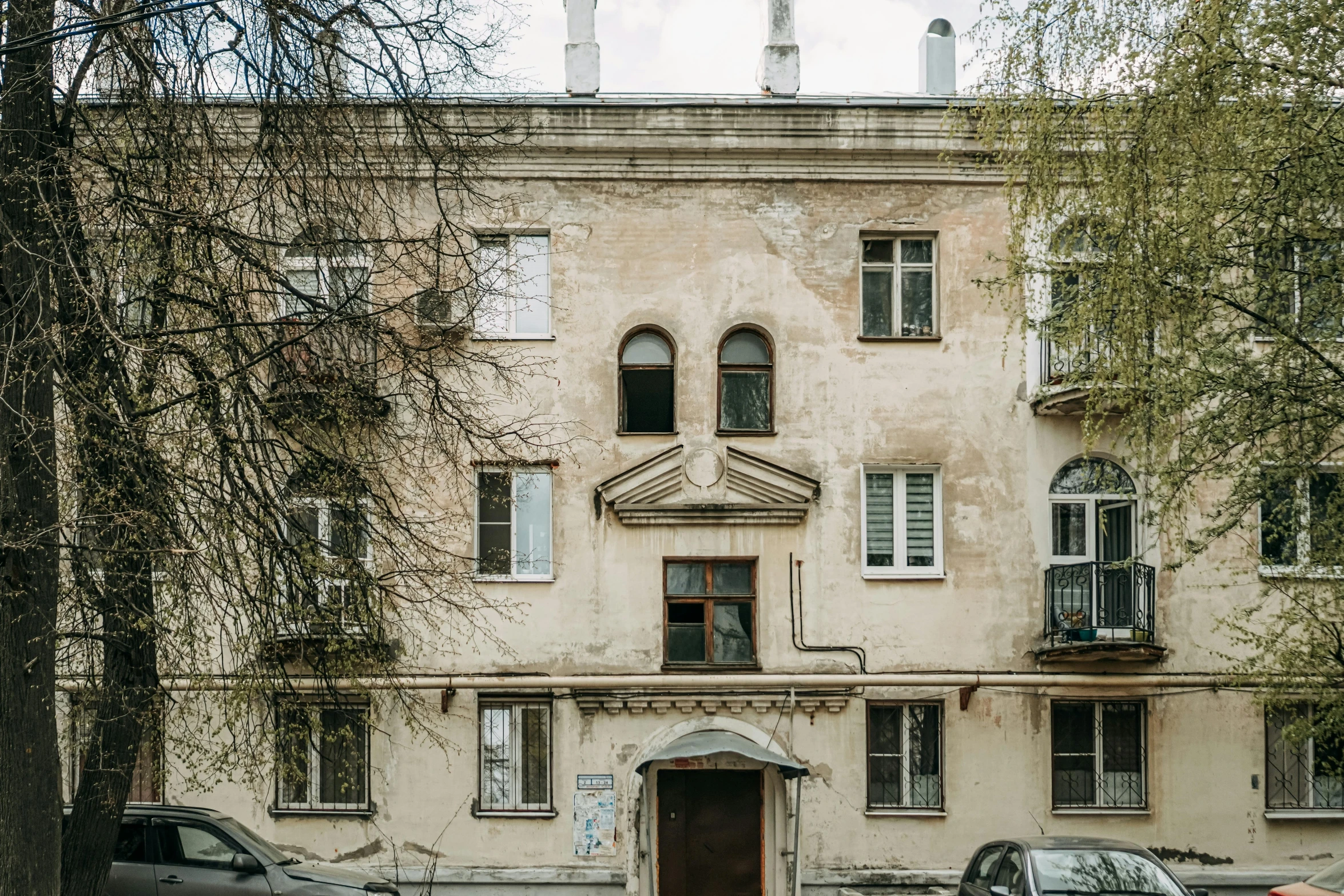 an old building with cars parked on the side and people walking by