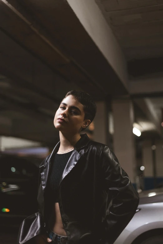 a woman in leather and a black jacket is next to a silver car