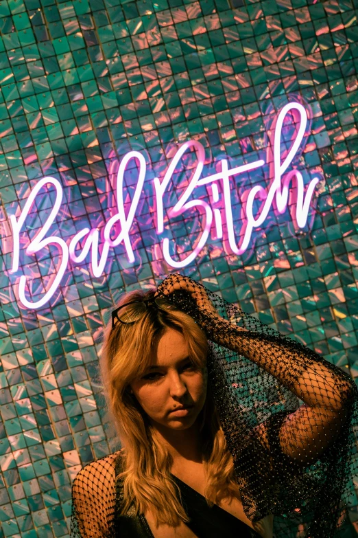 a woman stands in front of the bad bitch neon sign