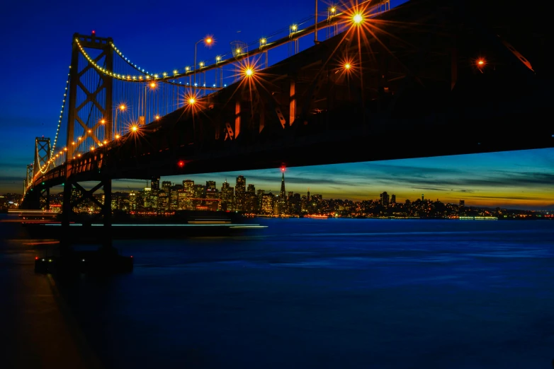 the lights of traffic under the bridge glow on the dark water