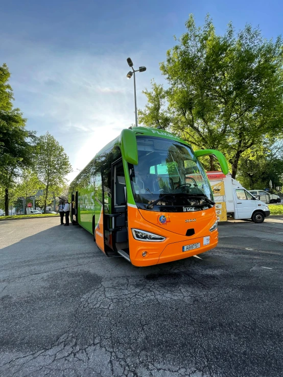 an orange and green bus in parking lot next to trees