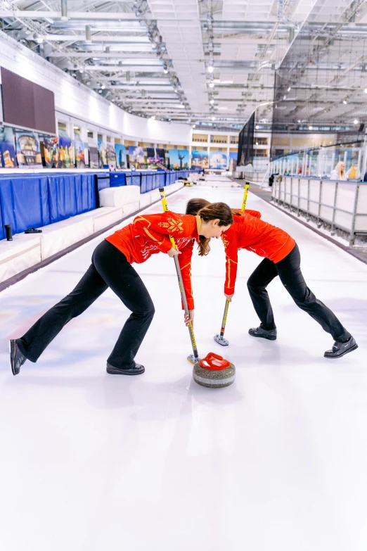 a pair of women are hing the ice on a curling rink