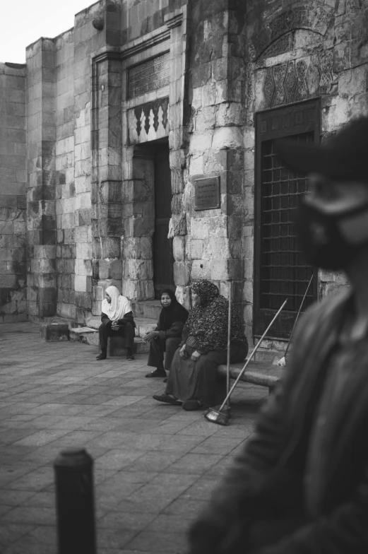 some men sitting on benches by a stone building