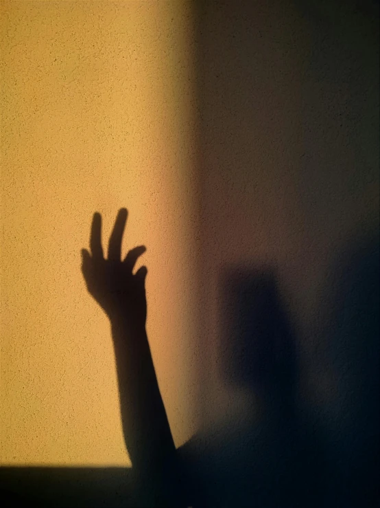 a shadow cast from the wall behind an open hand on a window