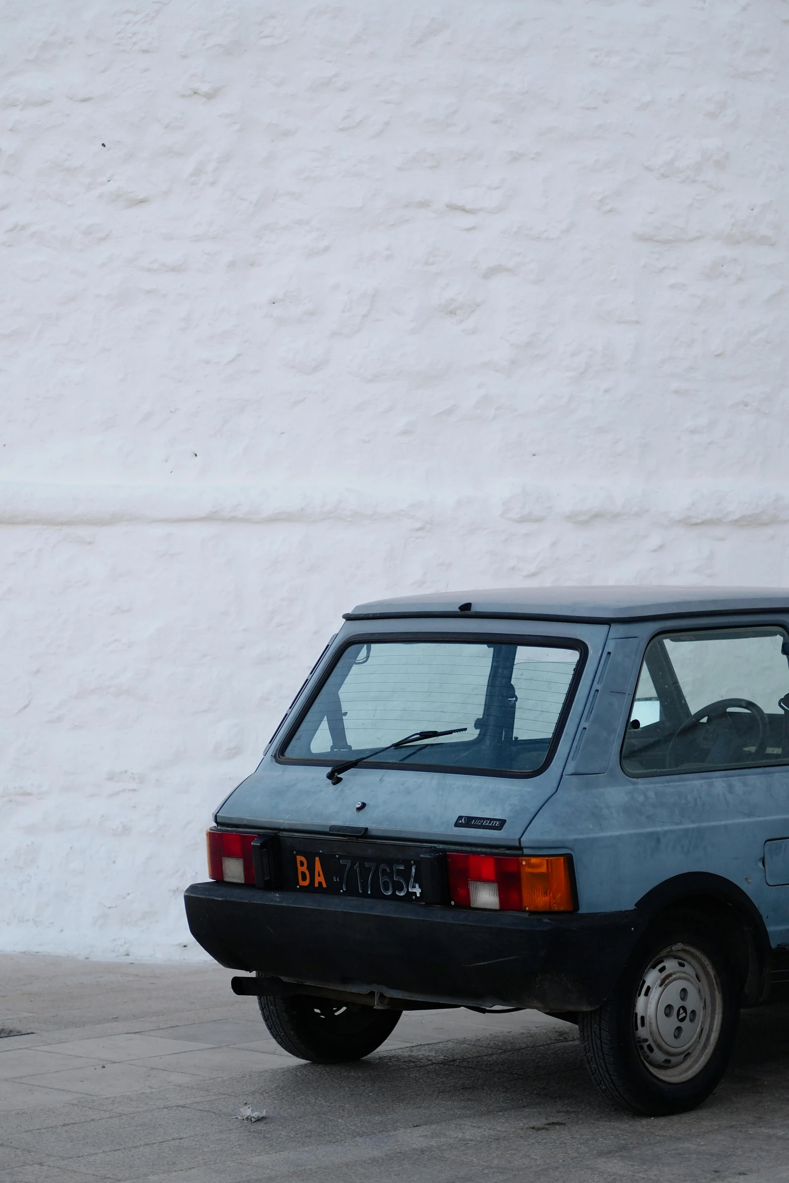 a small blue car is parked in front of a white wall