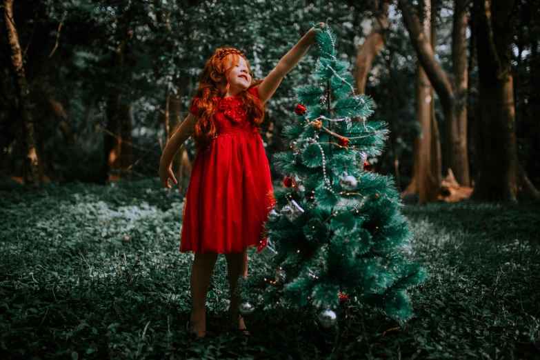 a  in a red dress is posing with a green christmas tree