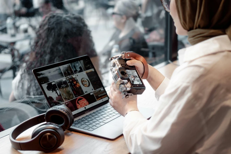 woman holding up a camera while working on her laptop