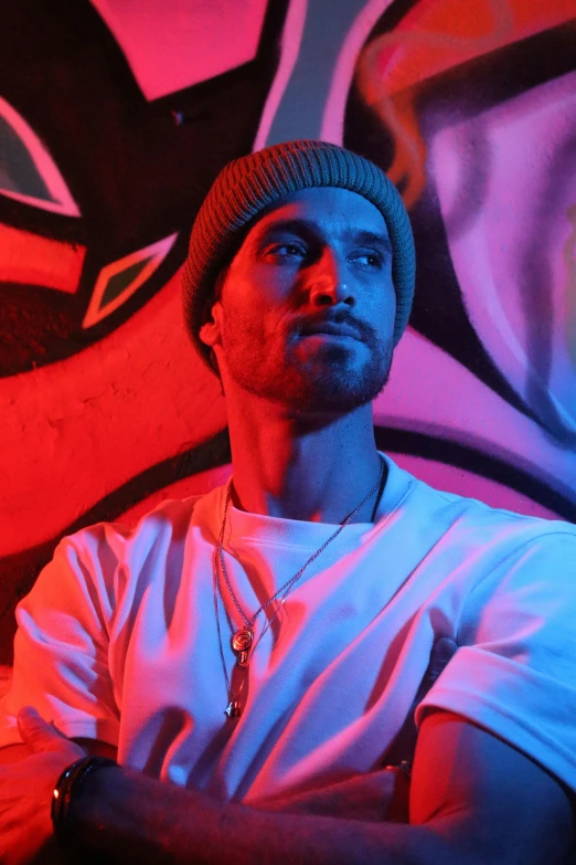 a young man wearing a beanie and sitting in front of a mural