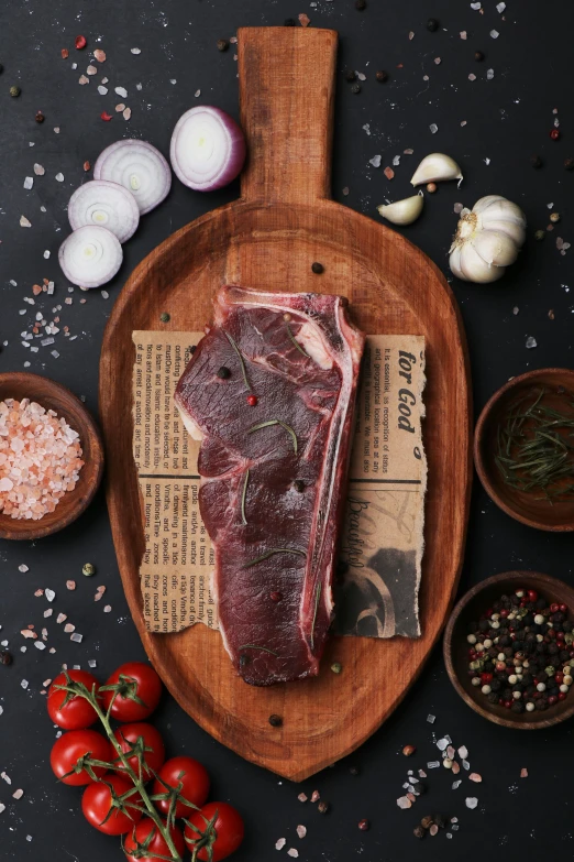 raw meat is placed on a  board beside spices, garlic and tomatoes