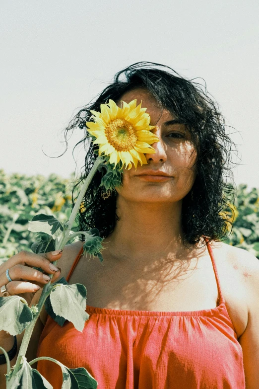 a woman wearing an orange top holds a sunflower