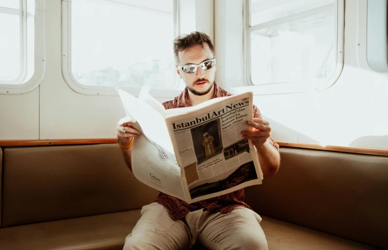 a man in glasses reading a newspaper while sitting on a bench