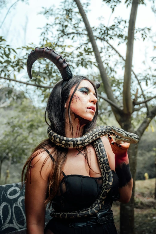a woman wearing horned head makeup and holding a snake