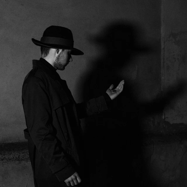 man in black suit with long sleeves and hat looking off into distance