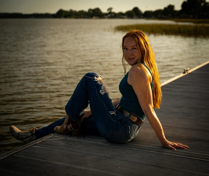 a beautiful woman sitting on the end of a dock next to the water