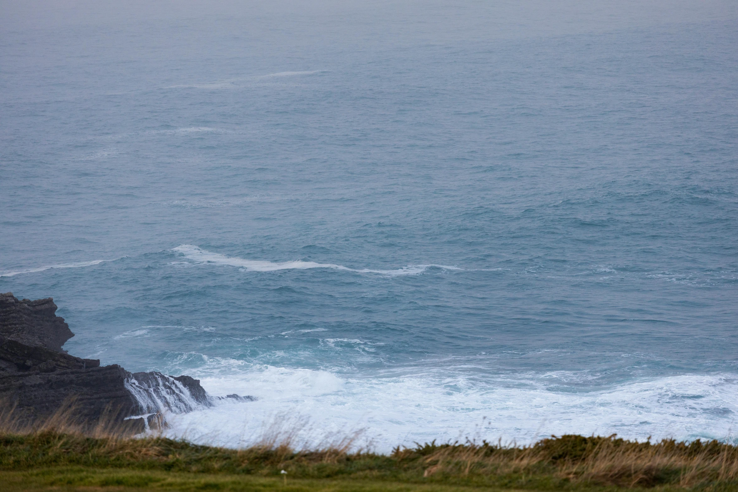 an open grassy area with waves crashing against the rocks