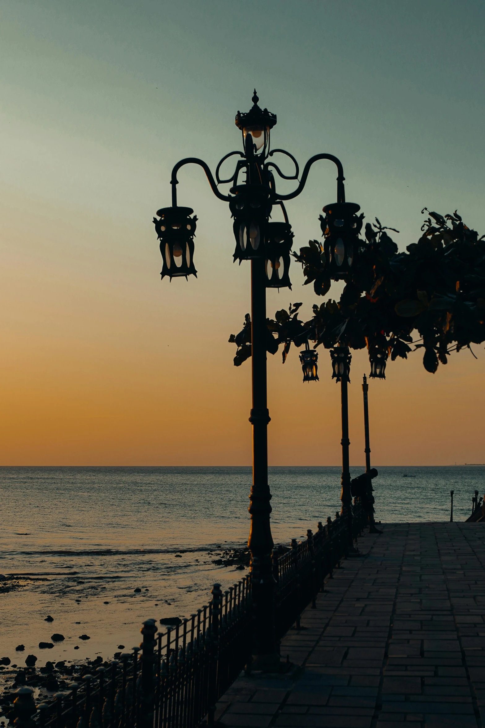 a view of the ocean from a sidewalk lined with lamps