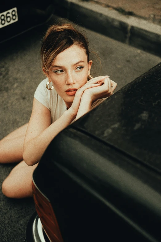 a young woman sits leaning on a vehicle