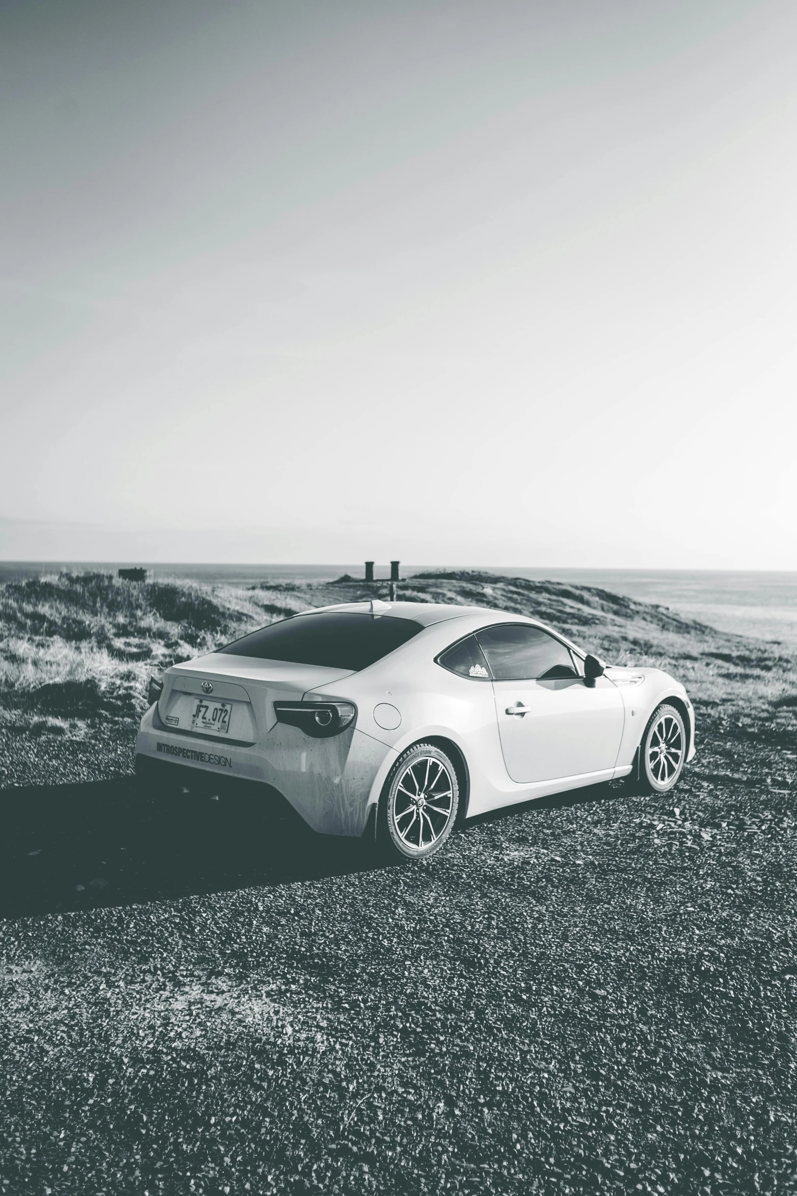 a sports car sitting in a grassy field with the ocean behind it