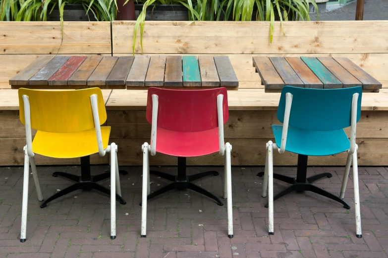 three multicolored chairs next to each other in front of wooden tables
