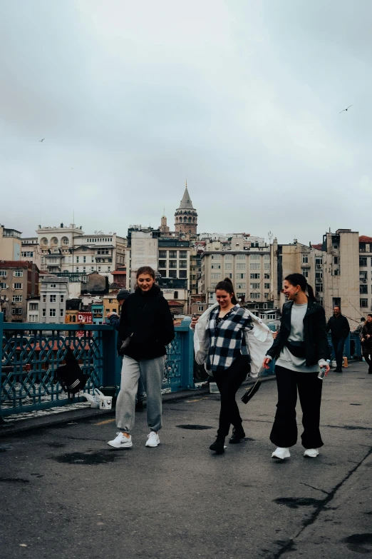 three girls on a bridge with buildings in the background