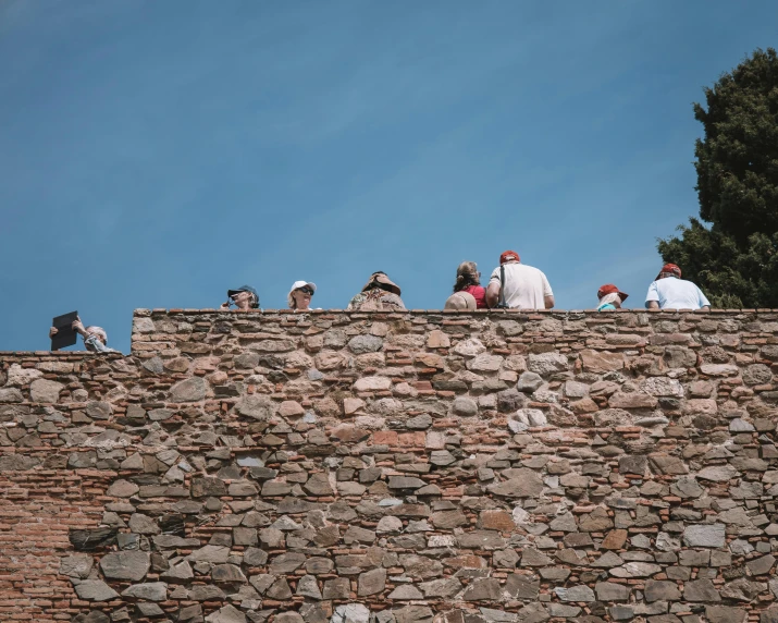 group of people sitting on a brick wall looking out over the top