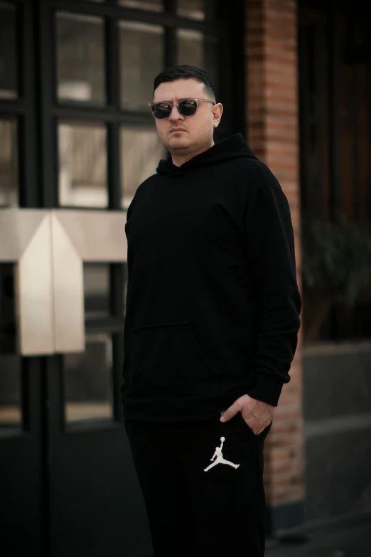 a man wearing sunglasses and a black hoodie poses for the camera